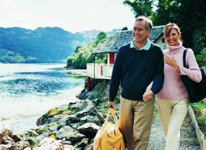 Mature Couple Walking Hand in Hand and Laughing Together Beside a Lake